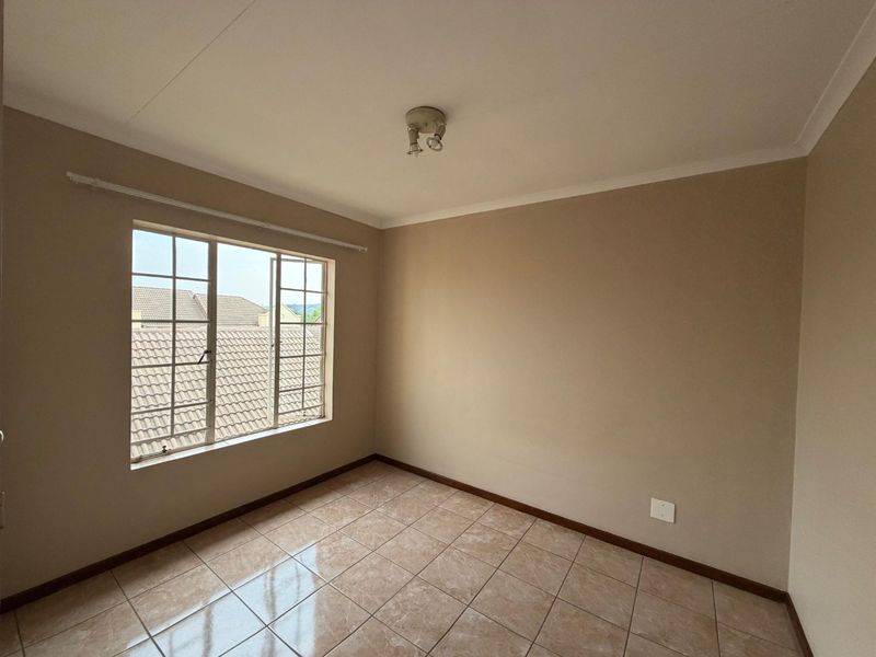 A clean, empty bedroom featuring neutral wall paint, tiled flooring, and a window with security bars, offering a blank canvas for personalization.