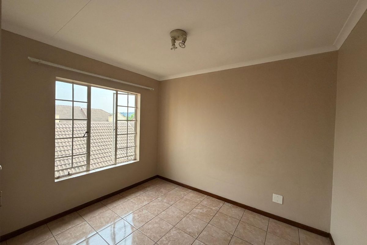 A clean, empty bedroom featuring neutral wall paint, tiled flooring, and a window with security bars, offering a blank canvas for personalization.