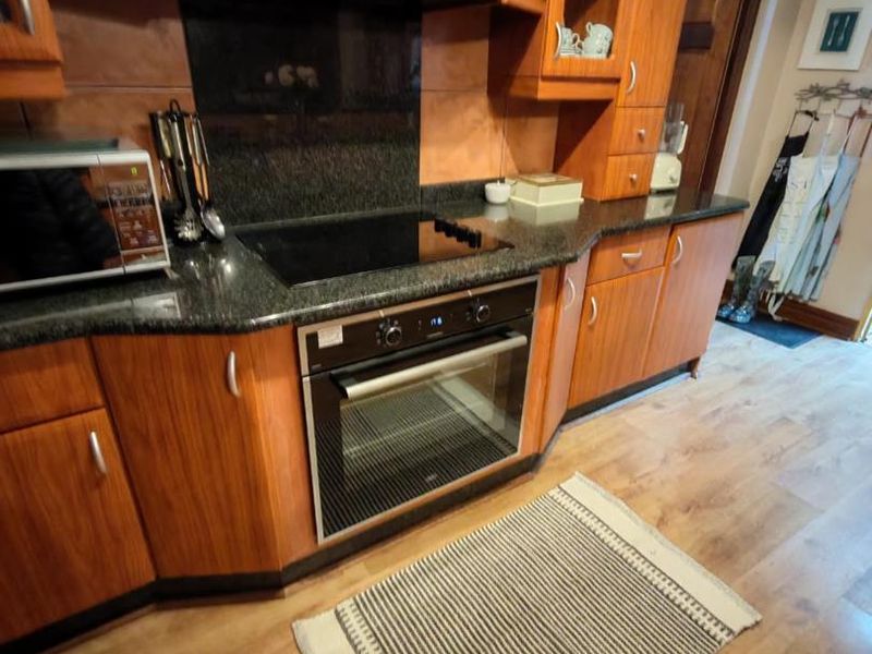 A functional kitchen featuring warm-toned wooden cabinetry, granite countertops, a built-in oven, and an electric hob with an integrated extractor fan.