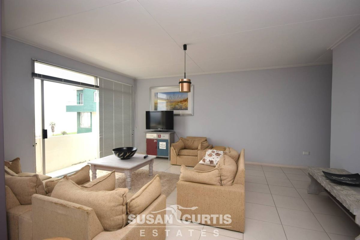 A spacious living room featuring neutral tiled flooring, large sliding glass doors leading to a balcony, and a modern pendant light fixture.