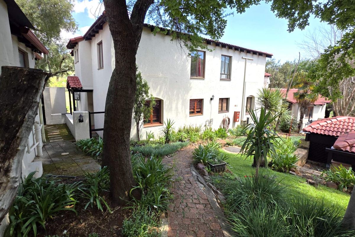 A view of the rear exterior of the apartment building, featuring a landscaped garden, brick pathway, and traditional terracotta roof tiles.