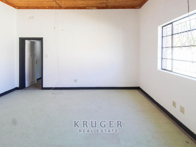 An empty living room featuring a timber ceiling, white walls, and security bars on the window, providing a blank canvas for renovation.