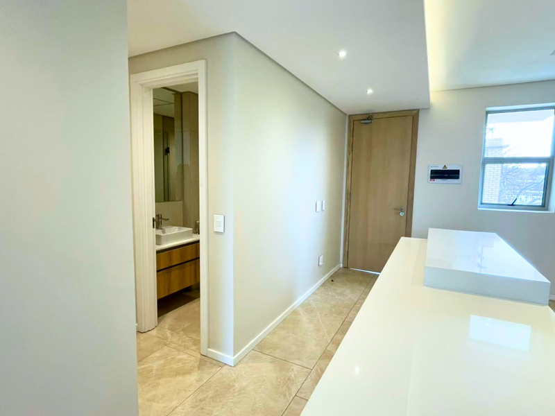 Modern open-plan apartment interior featuring a sleek kitchen island, tiled flooring, recessed lighting, and direct access to a contemporary bathroom.