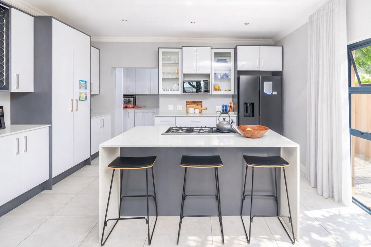 Modern kitchen featuring a central island with a gas hob, sleek two-tone cabinetry, stone countertops, and an adjacent scullery area.