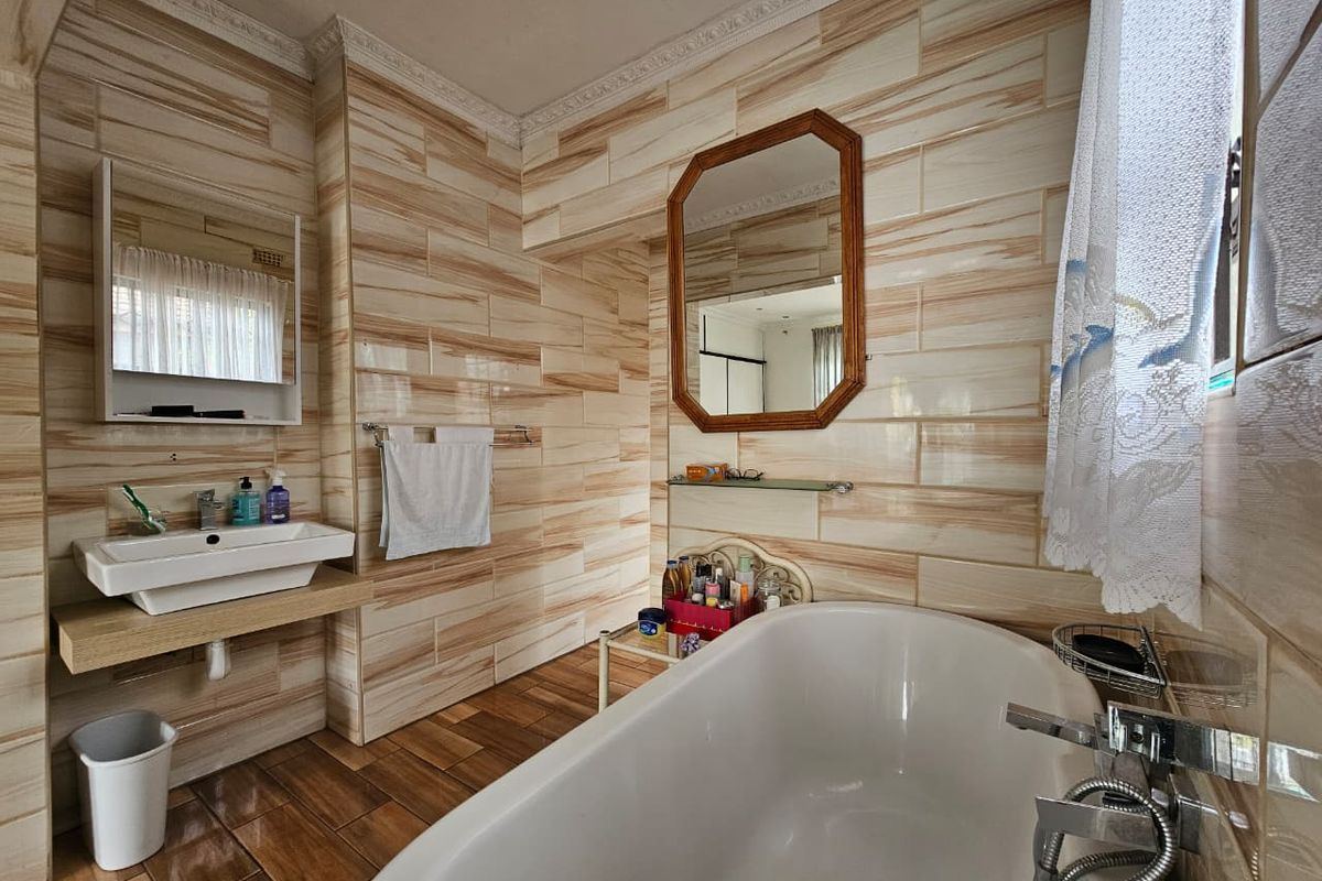 A bathroom featuring a freestanding bathtub, wall-mounted basin with wooden vanity shelf, and full-height decorative wall tiling.