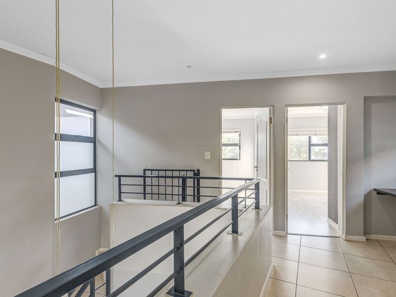 A bright and spacious upper-level landing area featuring modern metal balustrades, neutral wall tones, and tiled flooring, providing access to adjacent bedrooms.