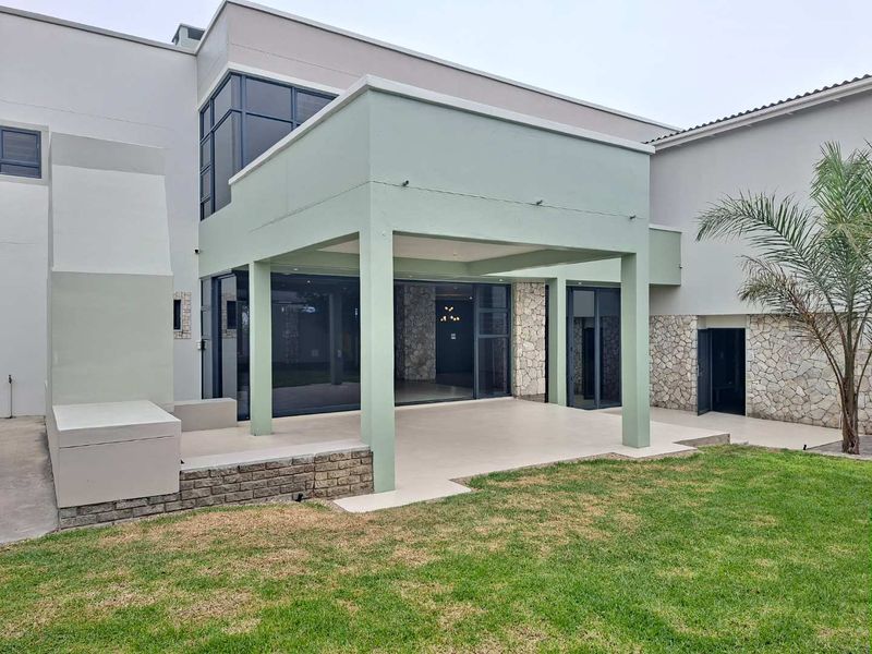 A spacious covered patio featuring stone cladding, modern sliding glass doors, and recessed lighting, providing a seamless transition to the rear garden area.