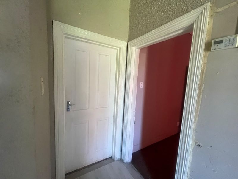 A hallway area featuring an alarm system keypad and internal doors, showing signs of wear and requiring cosmetic attention to wall finishes and trim.