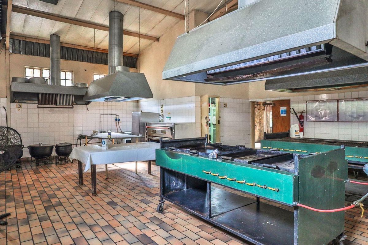 A large industrial-style commercial kitchen featuring multiple stainless steel extractor hoods, heavy-duty cooking stations, and tiled flooring, suitable for high-volume food preparation.