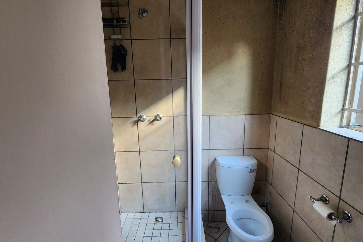 A compact bathroom featuring a tiled shower enclosure, a standard toilet, and a window with security bars.