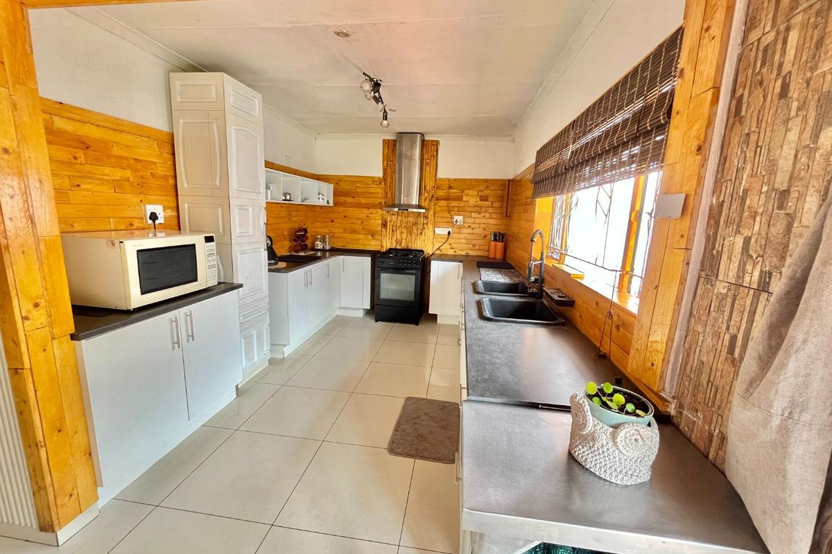 A functional kitchen featuring wooden wall cladding, tiled floors, built-in cabinetry, a double basin sink, and a stainless steel extractor fan.