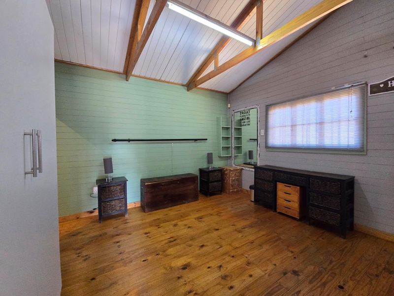 A bedroom featuring exposed timber roof trusses, timber wall cladding, and wooden flooring, offering a rustic aesthetic with built-in shelving.