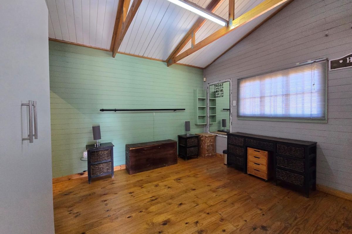 A bedroom featuring exposed timber roof trusses, timber wall cladding, and wooden flooring, offering a rustic aesthetic with built-in shelving.