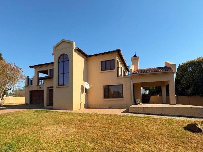Rear view of a double-story house featuring a covered patio, balcony, double garage, and paved driveway set against a large lawn.