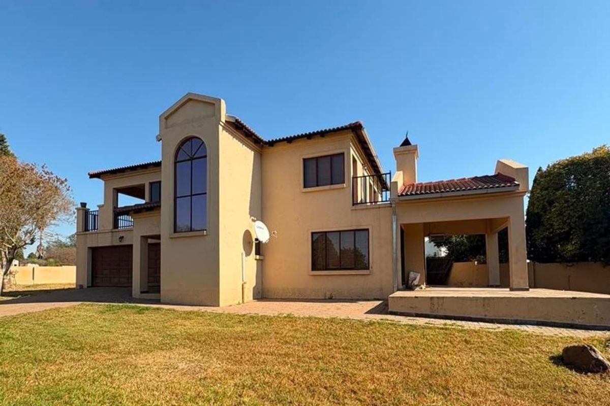 Rear view of a double-story house featuring a covered patio, balcony, double garage, and paved driveway set against a large lawn.