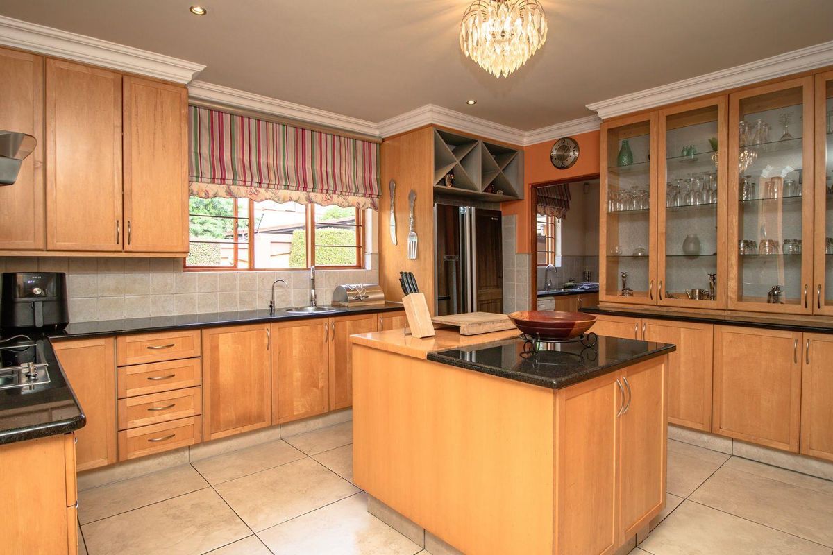 A spacious kitchen featuring light wood cabinetry, granite countertops, a central island, and integrated glass-front display cabinets.
