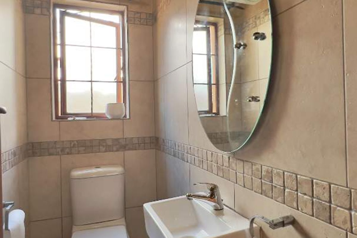 A compact guest bathroom featuring floor-to-ceiling neutral tiling, a wall-mounted basin, a modern toilet, and a decorative mosaic tile border.