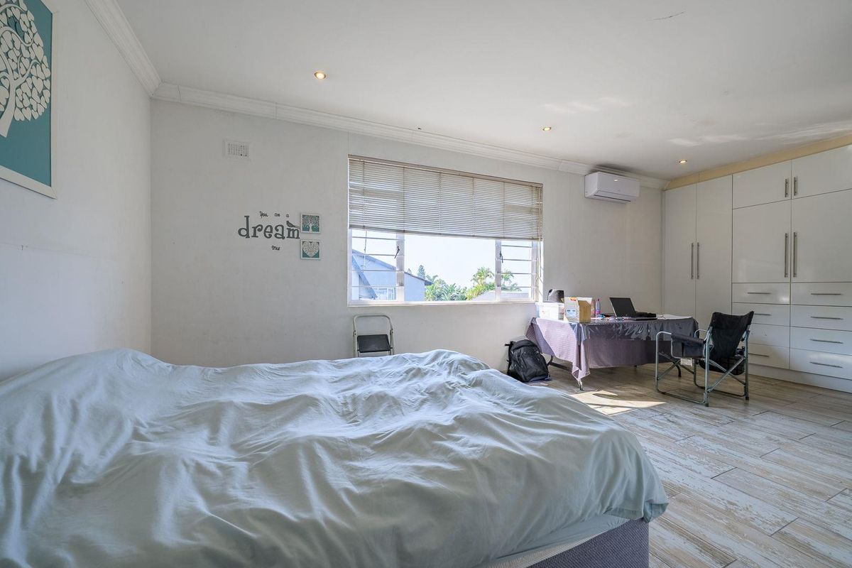 A spacious bedroom featuring built-in cupboards, tiled flooring, recessed downlighting, and an air conditioning unit, offering a functional and well-lit living space.