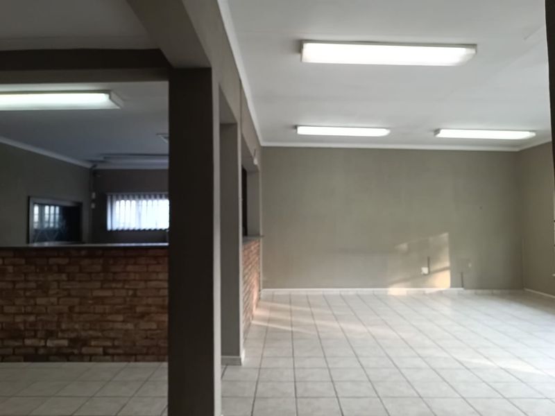 An open-plan office space featuring tiled flooring, a brick feature wall, and overhead fluorescent lighting, offering a versatile layout for professional use.