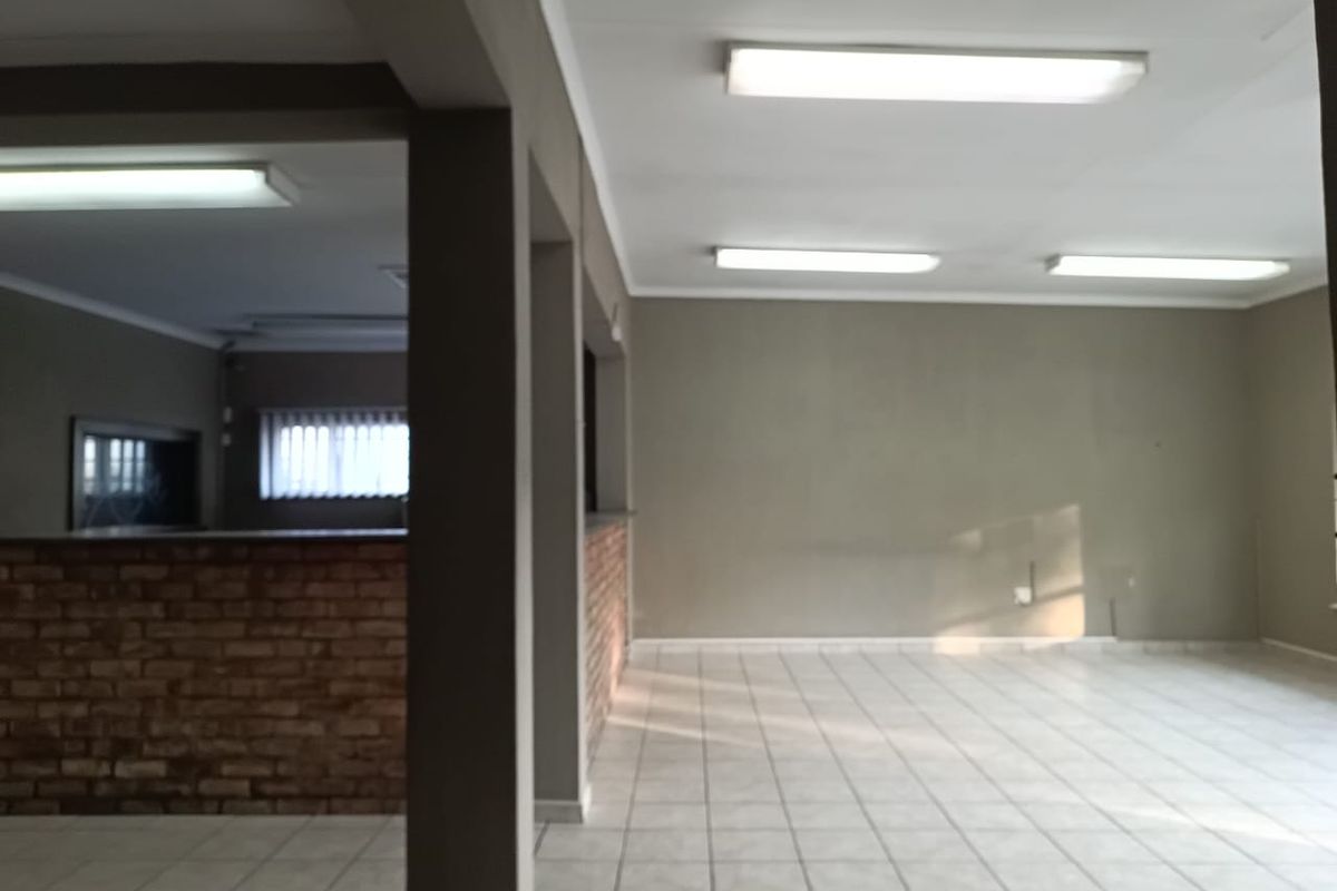 An open-plan office space featuring tiled flooring, a brick feature wall, and overhead fluorescent lighting, offering a versatile layout for professional use.