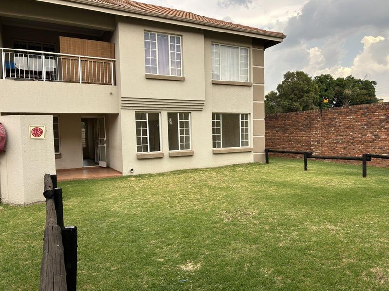 Rear view of a two-story townhouse featuring a private garden, lawn, brick boundary wall, and an upper-level balcony with metal railings.