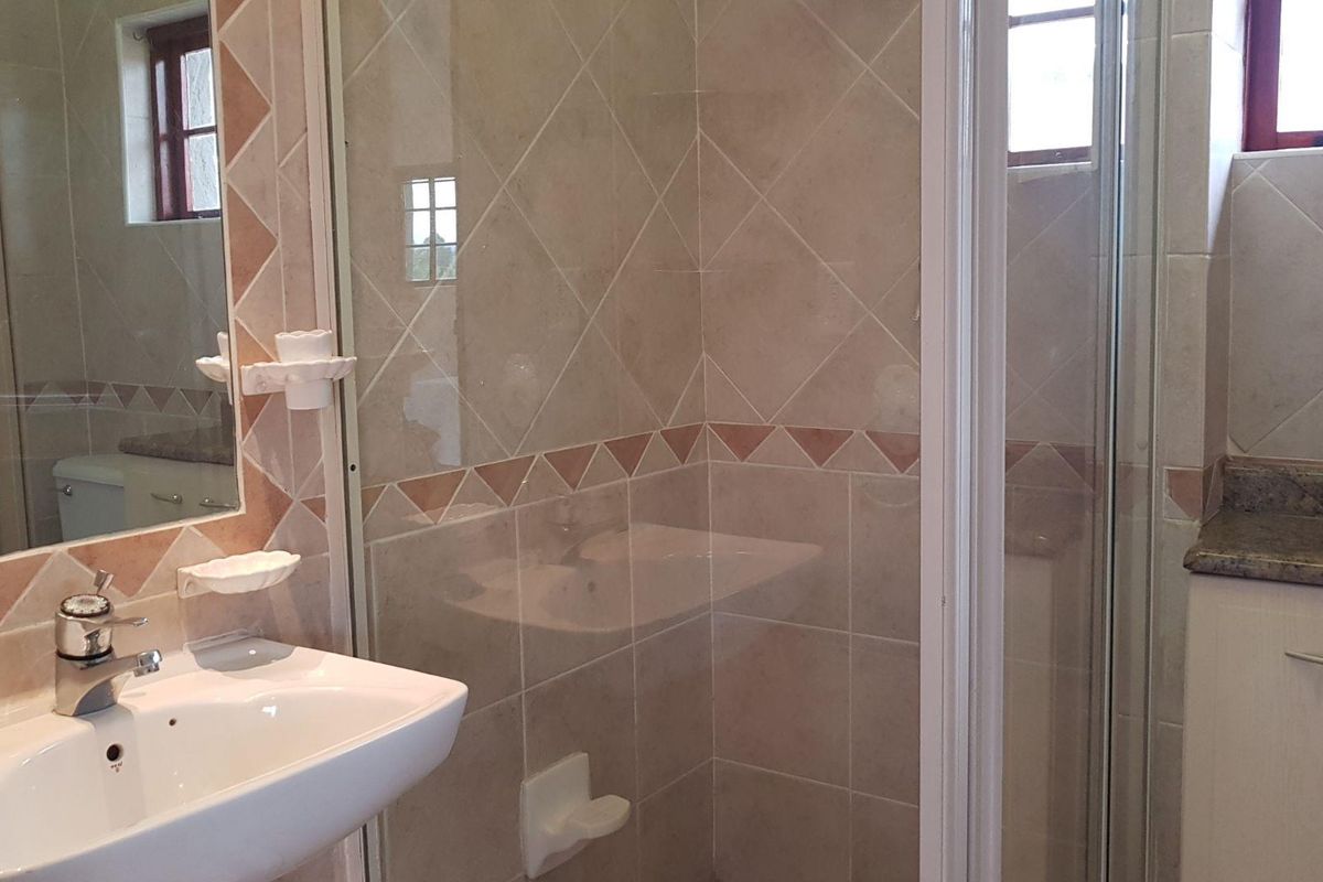 A functional bathroom featuring a glass-enclosed shower, vanity basin with mirror, and neutral wall tiling.