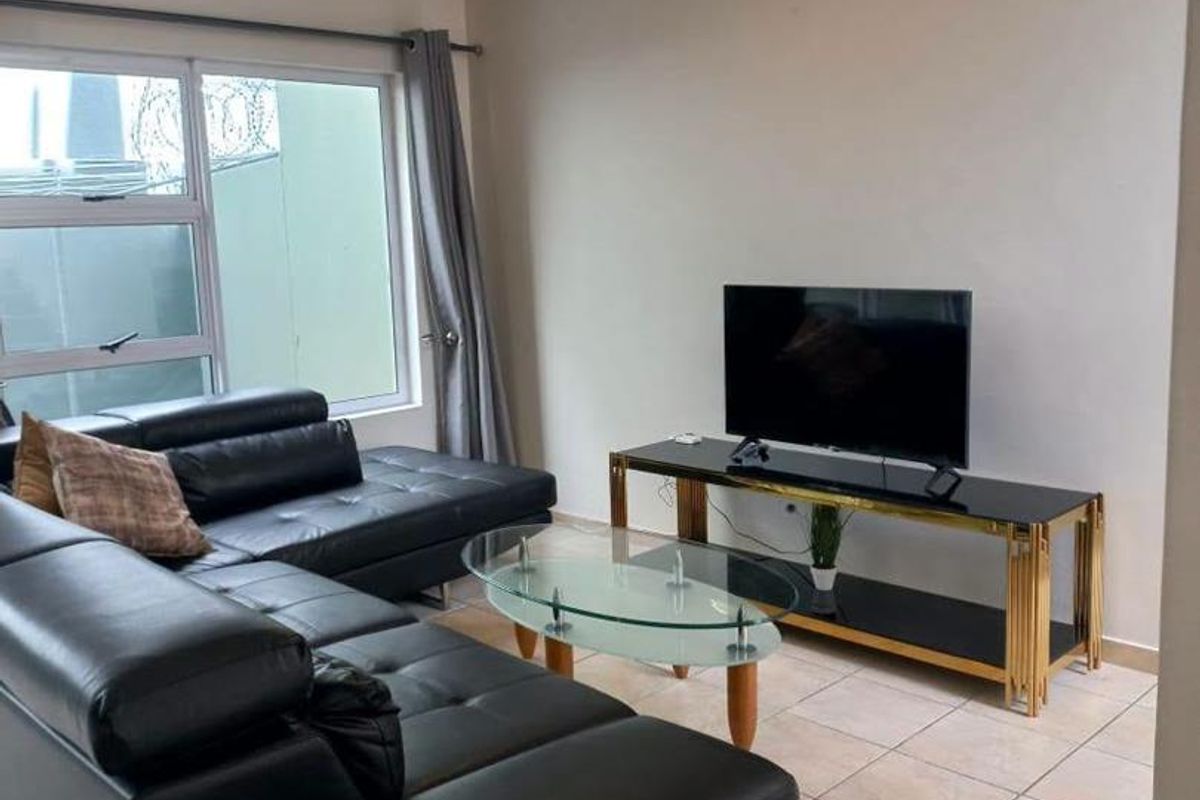 A functional living room featuring neutral tiled flooring, a large window with aluminium frames, and a standard flush mount ceiling light fixture.
