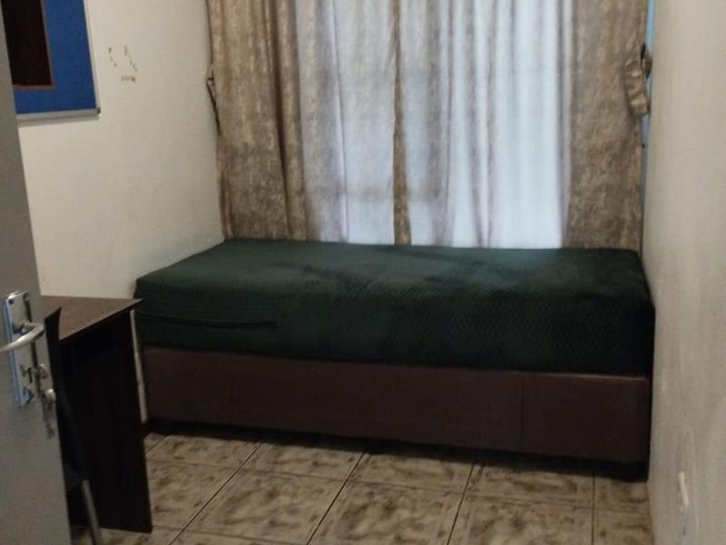 A compact bedroom featuring tiled flooring and window curtains, requiring minor cosmetic updates to improve the overall presentation.