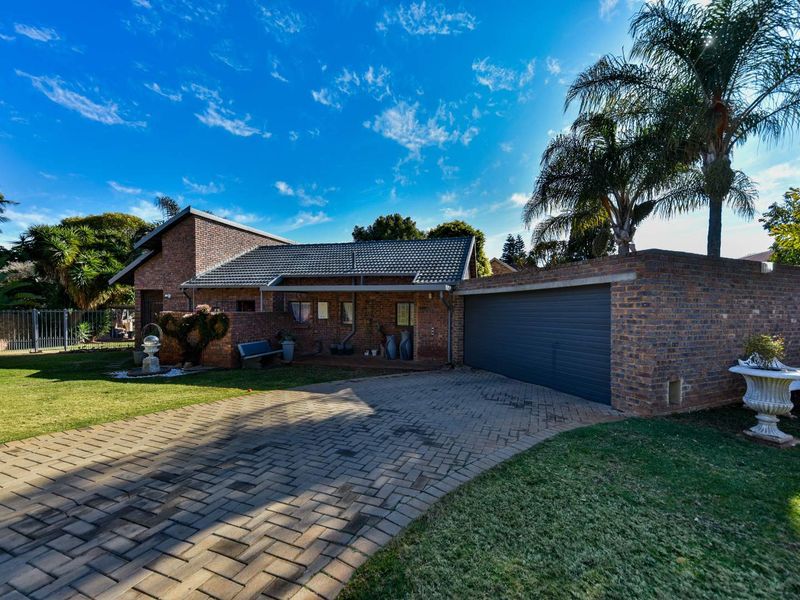 Front view of a well-maintained brick house featuring a paved driveway, attached garage, and established garden.