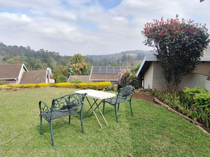 A well-maintained rear garden area featuring a lawn, established shrubbery, and scenic views of the surrounding neighbourhood and hills.