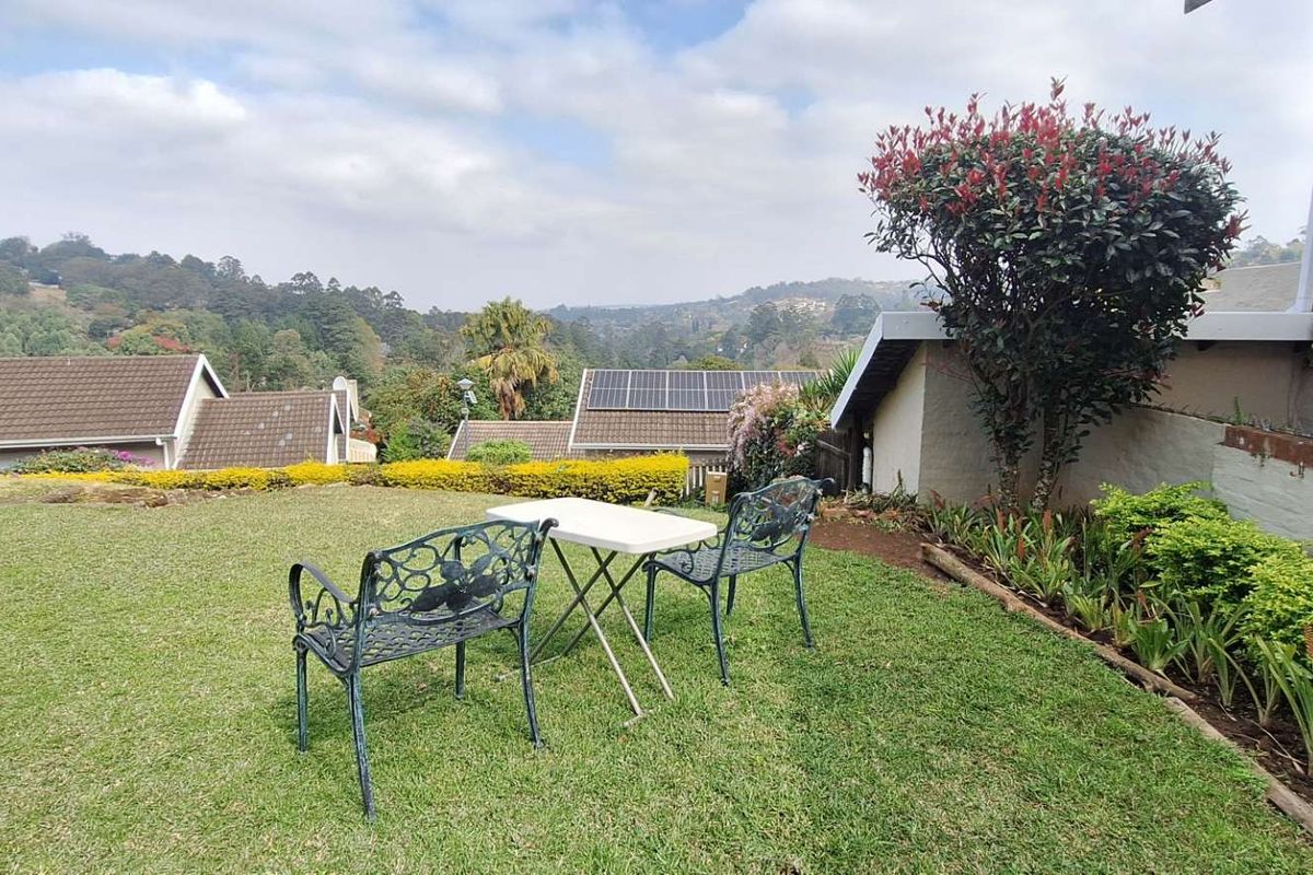 A well-maintained rear garden area featuring a lawn, established shrubbery, and scenic views of the surrounding neighbourhood and hills.