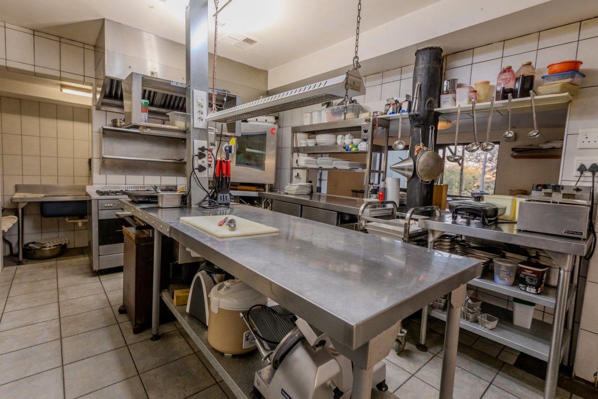 Commercial-grade kitchen featuring stainless steel work surfaces, industrial extractor fan, built-in oven, and tiled flooring, designed for high-volume food preparation.