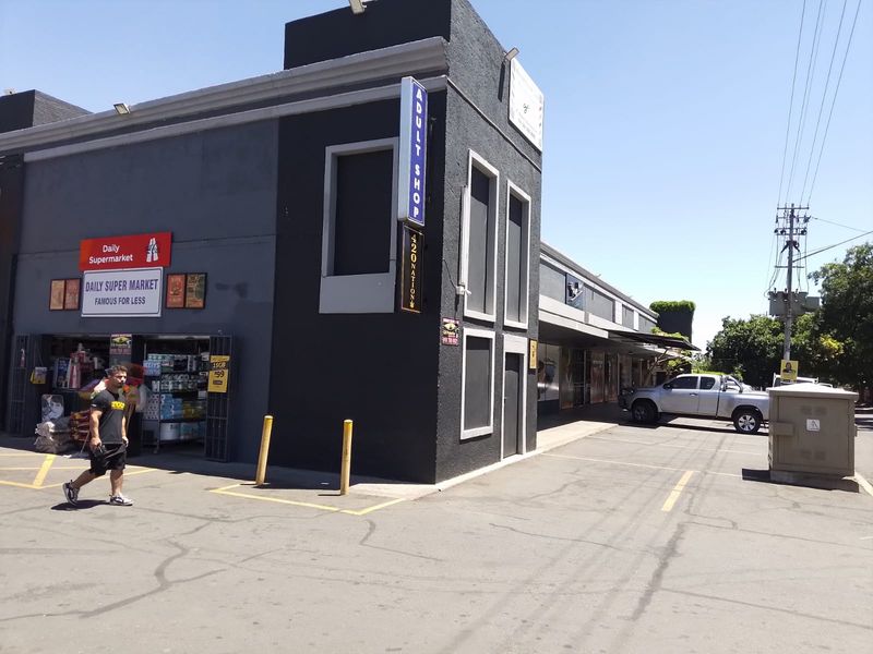 Exterior view of a retail property featuring a paved parking area, commercial signage, and security bollards in a street-facing location.