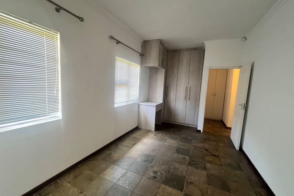 An empty bedroom featuring built-in cupboards, a built-in desk, tiled flooring, and venetian blinds.