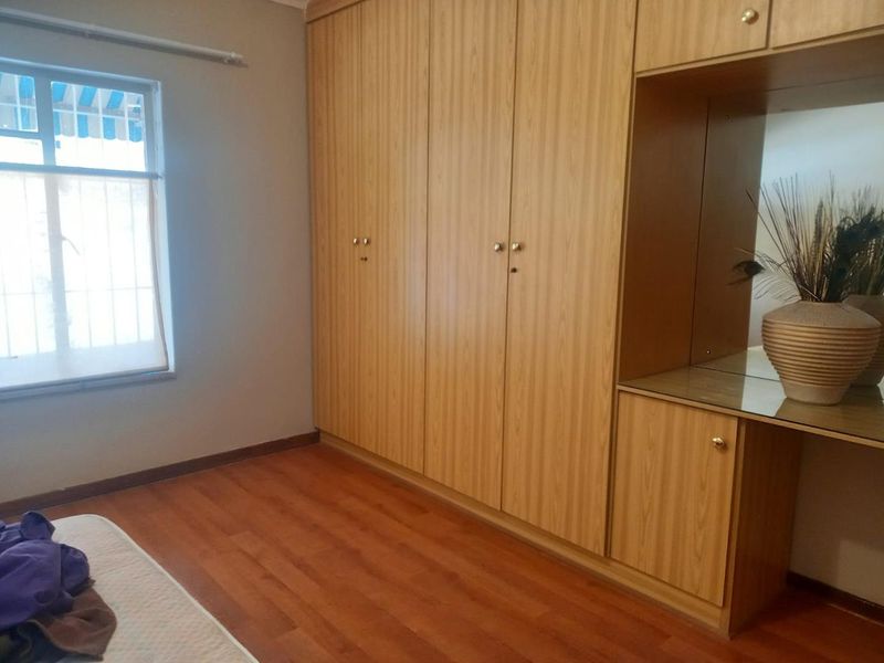 A bedroom featuring extensive built-in wooden cupboards with an integrated vanity area, laminate flooring, and a window with security bars.