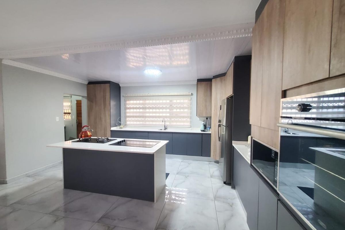 Modern kitchen featuring a central island, built-in oven, integrated cabinetry, and marble-look floor tiles.