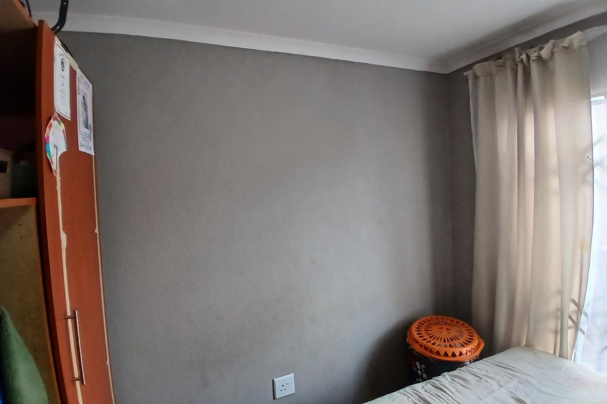A bedroom featuring grey painted walls, a built-in cupboard, and a window with curtains.