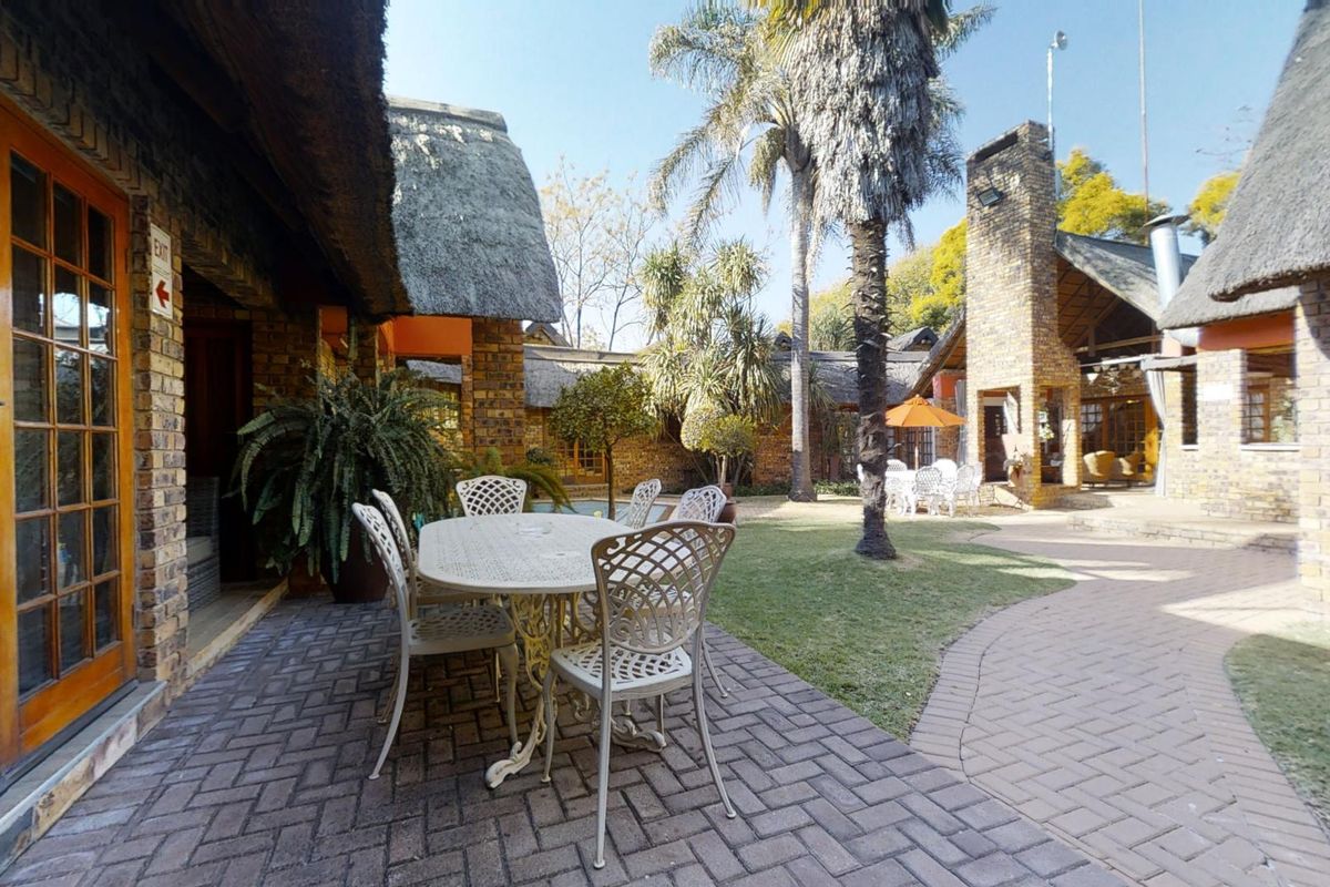 A spacious outdoor courtyard featuring a paved patio area, manicured lawn, and traditional thatch-roofed brick buildings, ideal for business or hospitality use.