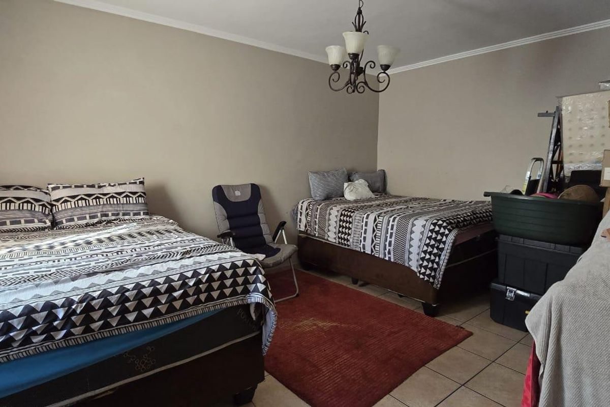 A bedroom featuring tiled flooring and a central chandelier, currently utilized with multiple beds and storage items.