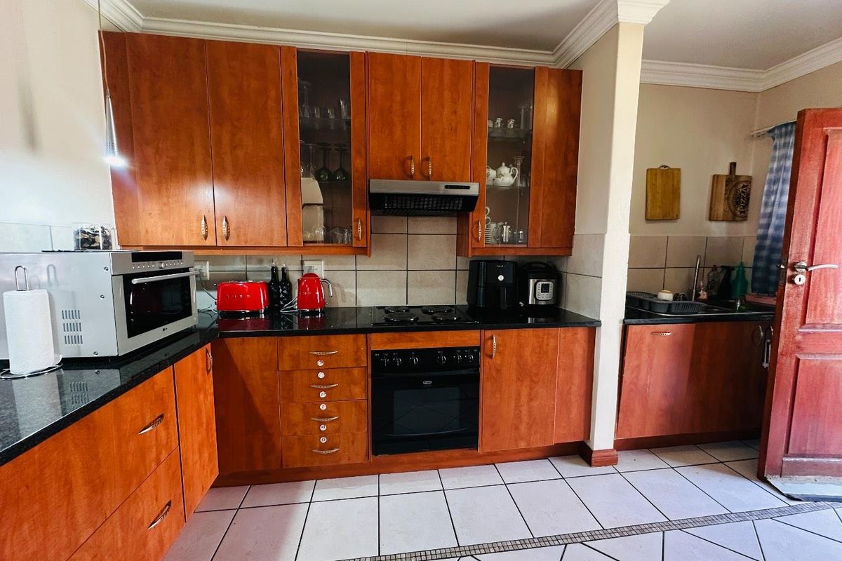 A functional kitchen featuring warm-toned wooden cabinetry, granite countertops, built-in oven, and hob, complemented by tiled flooring and a classic tiled backsplash.