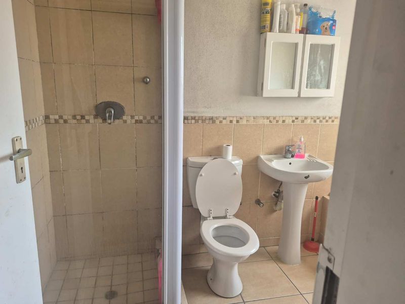 A functional bathroom featuring a shower enclosure, pedestal basin, toilet, and wall-mounted cabinet with neutral tiled finishes.