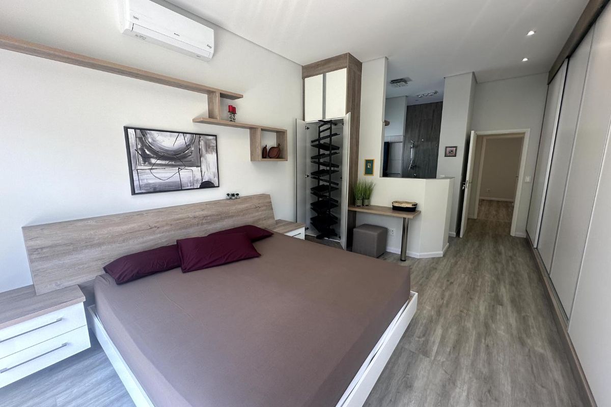 Modern bedroom featuring built-in cabinetry, integrated shelving, wood-look flooring, and an en-suite bathroom area with a glass-enclosed shower.