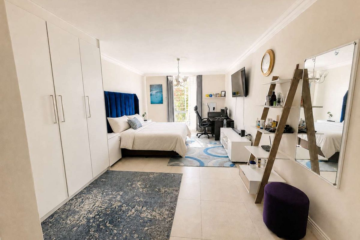 Spacious bedroom featuring neutral tiled flooring, extensive built-in cupboard storage, crown molding, and direct access to a balcony through a sliding door.