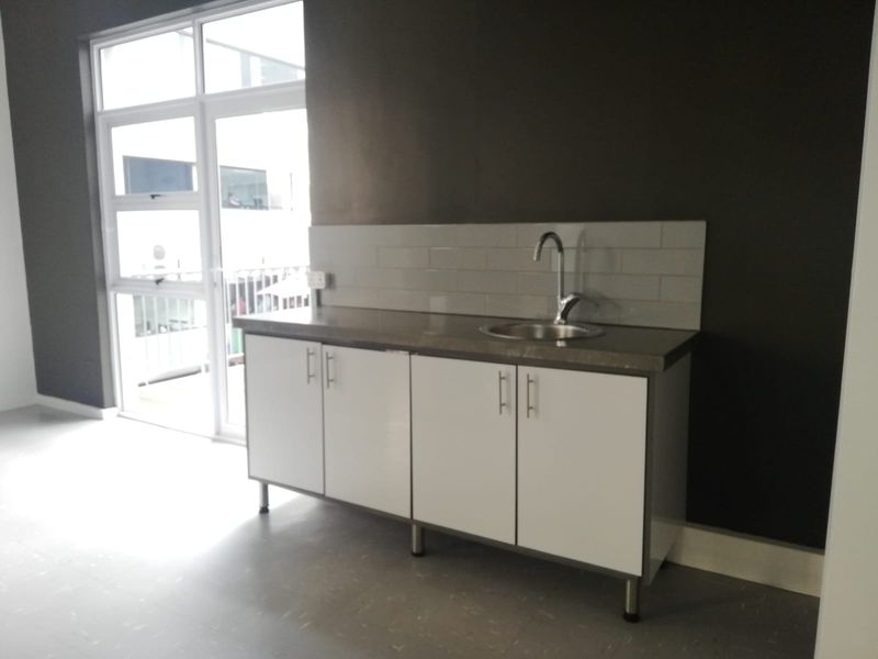 A compact kitchenette featuring white cabinetry, a stainless steel sink, and a subway tile backsplash, situated in an office space with natural light.