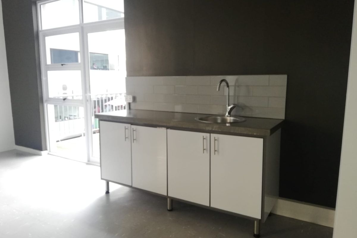 A compact kitchenette featuring white cabinetry, a stainless steel sink, and a subway tile backsplash, situated in an office space with natural light.