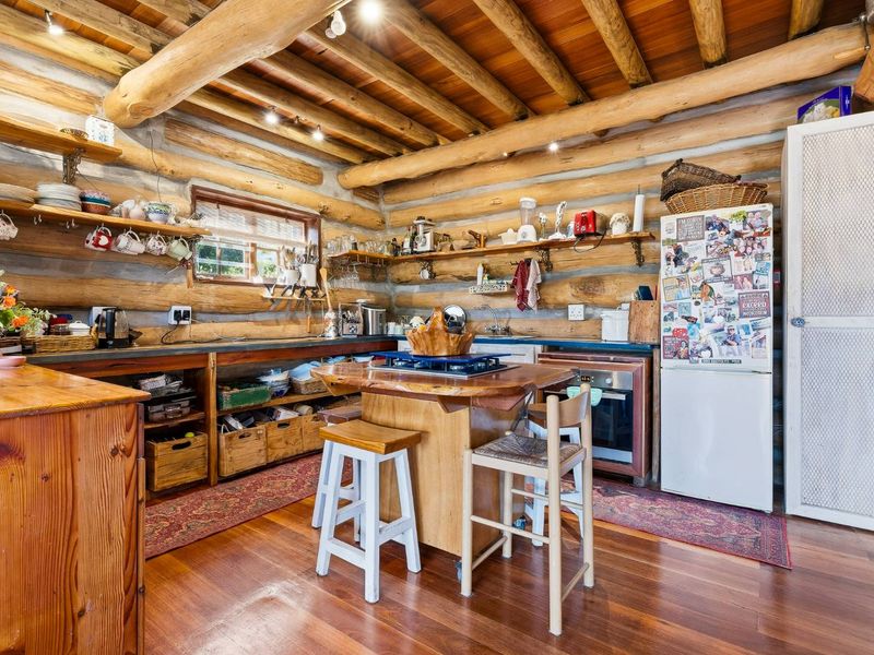 Rustic kitchen featuring exposed log walls, timber beam ceiling, hardwood flooring, and integrated cooking appliances with open shelving storage.