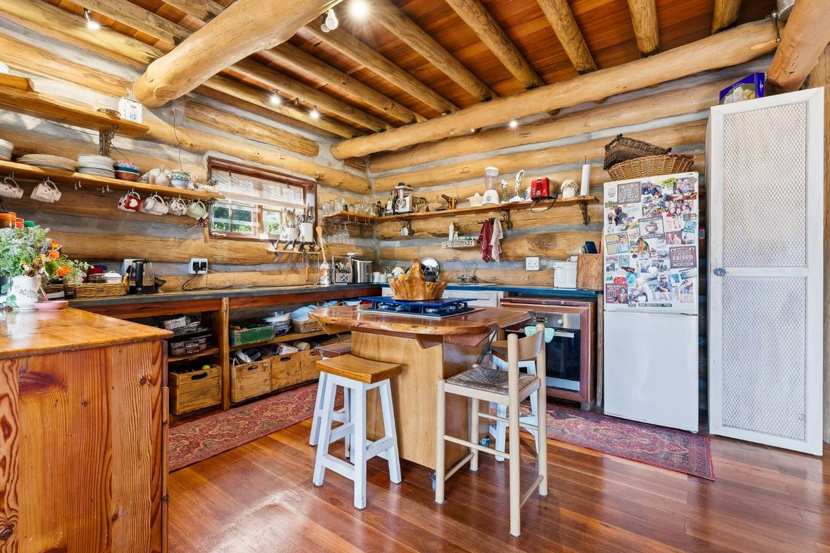 Rustic kitchen featuring exposed log walls, timber beam ceiling, hardwood flooring, and integrated cooking appliances with open shelving storage.