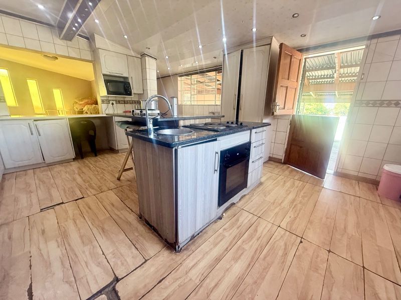 A functional kitchen featuring a central island with a built-in oven, hob, and sink, complemented by tiled surfaces and direct access to the exterior.
