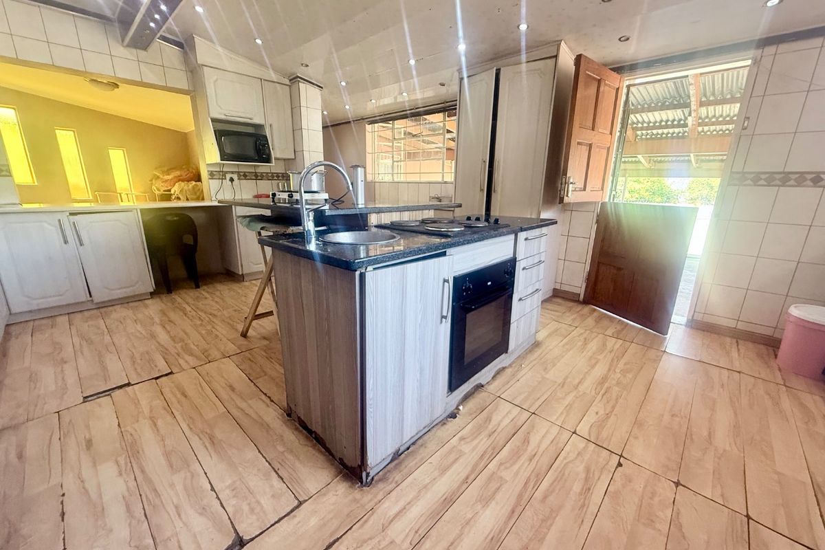 A functional kitchen featuring a central island with a built-in oven, hob, and sink, complemented by tiled surfaces and direct access to the exterior.