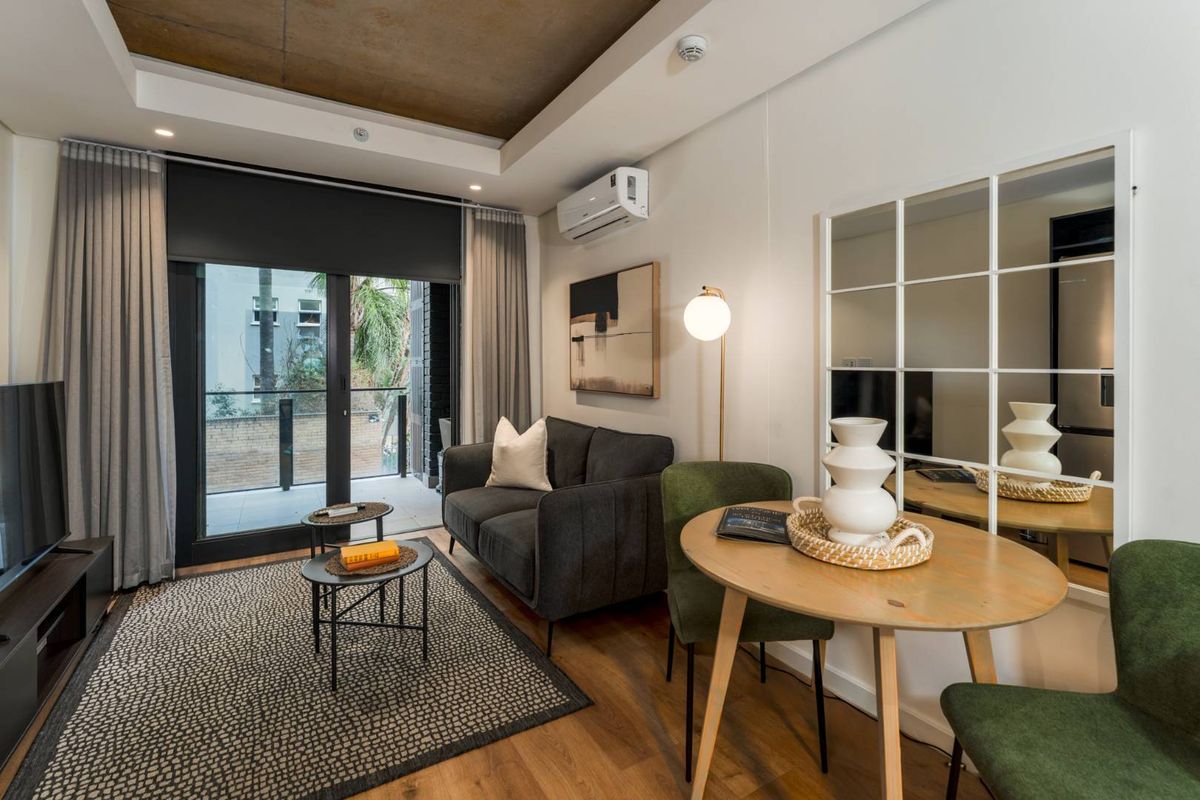 Modern living area featuring timber flooring, a recessed ceiling, and a sliding glass door providing access to a private balcony.